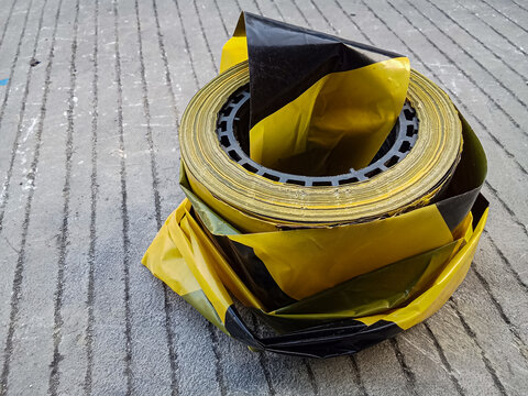 Full roll of black and yellow hazard tape on concrete pavement, essential safety supply for restricted area marking and accident prevention