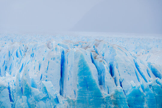 Blue glacier seracs below a dark mountain wall wrapped in mist, Patagonia, Argentina