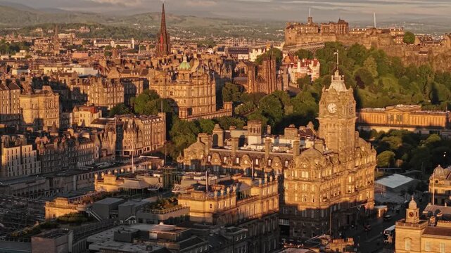 Aerial view of the historic Balmoral Hotel clock tower and Edinburgh Castle in the background during golden hour in Edinburgh, Scotland, United Kingdom.