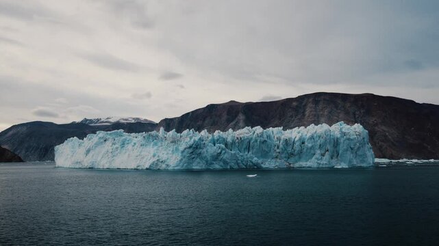 Massive blue iceberg floats in Franz Josef Fjord beneath Greenland mountains.