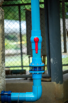 Vertical shot of a blue PVC water pipe system featuring a red ball valve handle and flange connection outdoors. Useful for plumbing, industrial utilities, and water management.