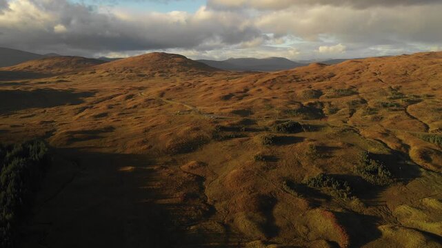 Aerial view of rolling moorland on the Isle of Skye under a dramatic cloudy sky during golden hour in Highland Council, Scotland, United Kingdom.
