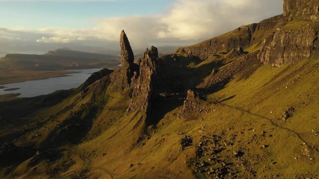 Aerial view of the Old Man of Storr rock formation with dramatic grassy slopes and golden hour light in Highland Council, Scotland, United Kingdom.