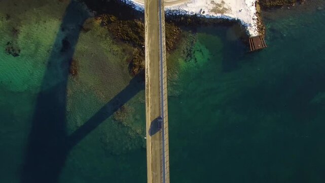 Aerial view of a car driving across a bridge over the clear turquoise waters of the Lofoten islands in Nordland, Norway.