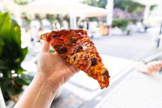 large fresh slice of pizza held in a hand at an outdoor dining area