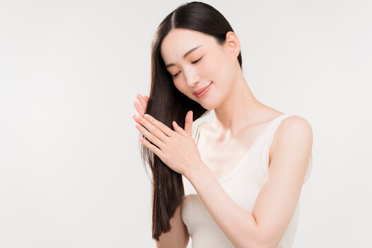 手ぐしで髪のお手入れをする黒髪ストレートヘアの日本人女性。ヘアケアイメージ。