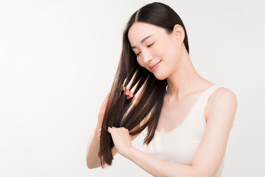 手ぐしで髪のお手入れをする黒髪ストレートヘアの日本人女性。ヘアケアイメージ。