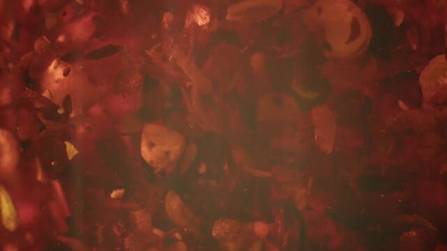 Abstract background featuring red dried herbal tea leaves floating and swirling in hot water inside transparent glass teapot.