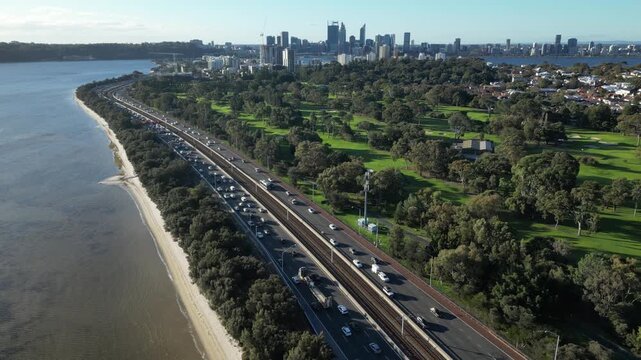Aerial drone footage of congested highway traffic flow beside parkland and cityscape skyline.