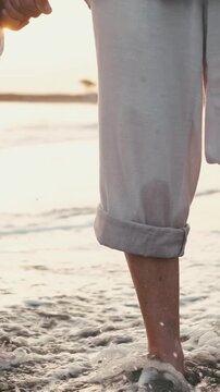 Close-up of a loving couple's bare feet walking together through the gentle ocean waves on a sandy beach during a beautiful, warm sunset, enjoying their romantic holiday getaway together