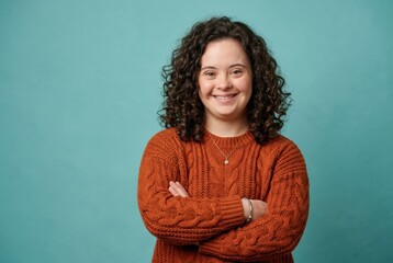 Obraz premium Confident Young Woman with Down Syndrome Smiling with Arms Crossed Against Teal Background