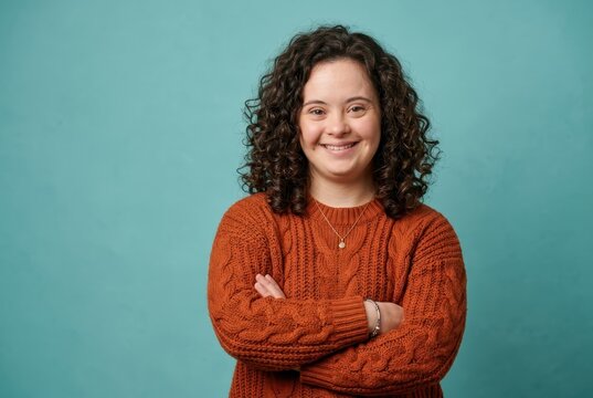 Confident Young Woman with Down Syndrome Smiling with Arms Crossed Against Teal Background