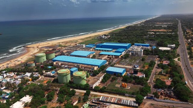 Aerial view of a desalination industrial plant with blue rooftops and storage tanks situated along the coastline in India.