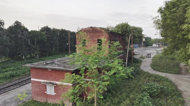 Overcast aerial flyover past old two storey red rail quarters and dirt footpath with people in rural India
