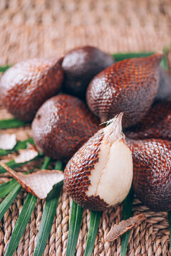 Red Salacca. Salak, snake fruits with palm leaves on rattan background. Copy space. Salacca zalacca. Closeup of salak palm fruits. Tropical travel, exotic fruit. Vegan and vegetarian concept