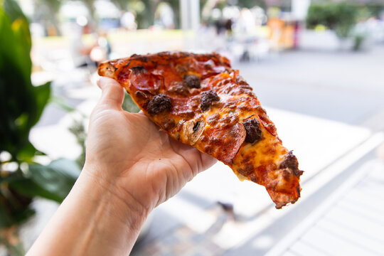 huge pizza slice held in a hand in an outdoor dining area