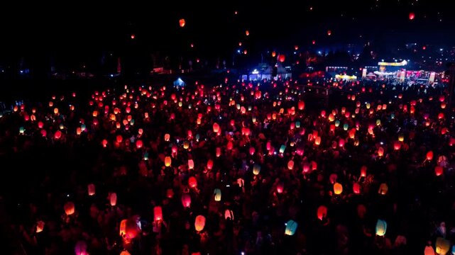 Aerial view of the Dieng Culture Festival at night with a large crowd releasing glowing lanterns into the dark sky in Indonesia.
