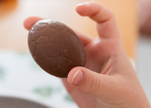 child holding a hollow chocolate easter egg between their fingers
