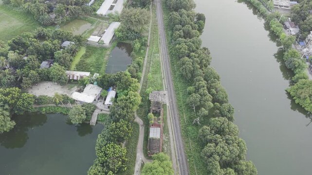 Jagati railway station between river and pond in lush rural Bangladesh, aerial drone flyover along tracks