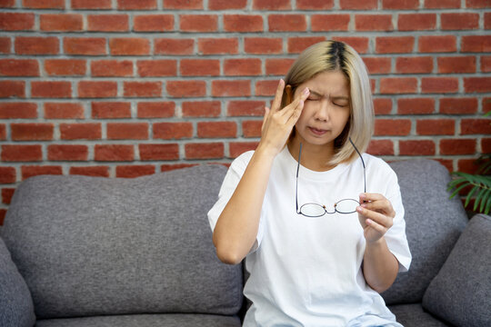 Young asian woman eye strain while sitting on a sofa. Concepts of health problems.