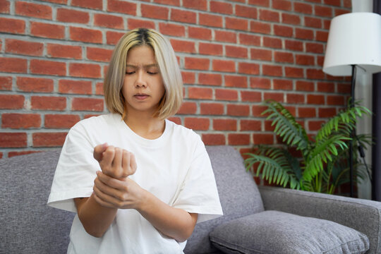 Asian woman has wrist pain and is sitting on a sofa. Concept Health problem