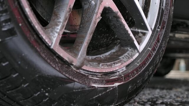 Cleaning car alloy wheels with purple chemical iron remover and detailing brush.