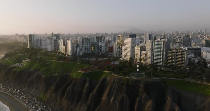 Aerial view of the Miraflores district featuring the iconic lighthouse, modern high-rise buildings, and lush green cliffs overlooking the Pacific Ocean in Lima, Callao Region, Peru.