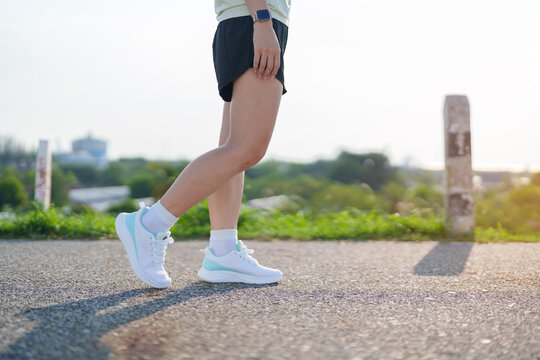 Young adult Asian woman jogging and walking in the park at morning. Female athlete in sport shoes running on the road with visible leg muscles. Healthy lifestyle, wellness and workout concept