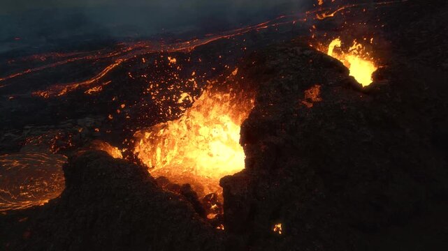 Aerial view of glowing lava fountain erupting from a volcanic crater with molten magma flowing over dark basaltic rock in ICELAND.