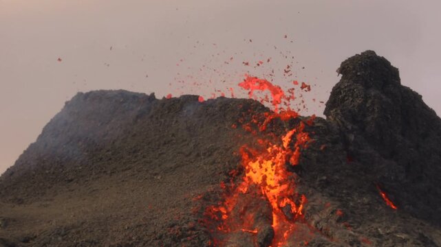 Aerial view of a volcanic eruption with glowing lava flowing down dark volcanic rock and smoke rising into the sky in Iceland.