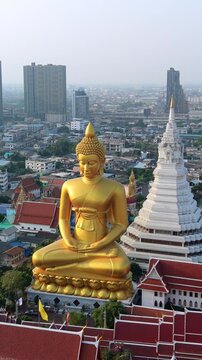 Aerial drone view of giant golden Buddha at Wat Paknam temple with Bangkok skyline in the background. Iconic religious landmark in Thailand.
