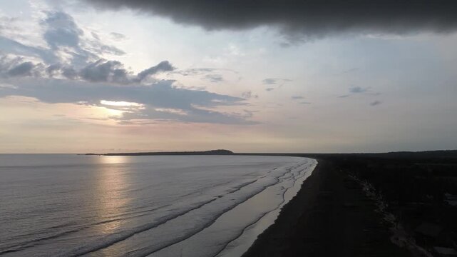 Aerial view of long coastline with calm ocean waves rolling onto sandy beach during sunset golden hour.