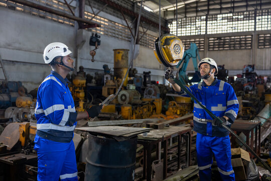 Diverse team of engineers worker using overhead crane hoist to carry raw materials inside metal sheet manufacturing factory for heavy industry usage