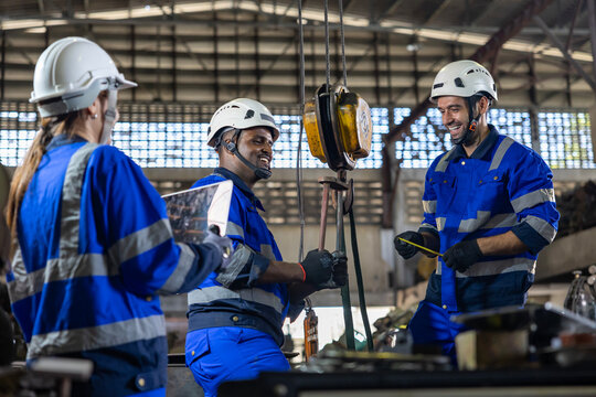 Diverse team of engineers worker using overhead crane hoist to carry raw materials inside metal sheet manufacturing factory for heavy industry usage