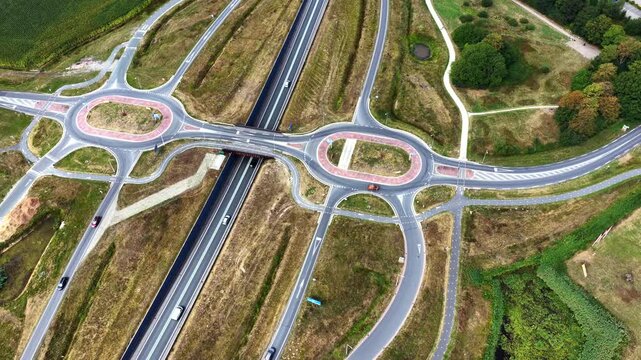 Aerial view of a modern highway interchange with dual roundabouts surrounded by green fields and rural landscape in Oosterwolde, Friesland, Netherlands.