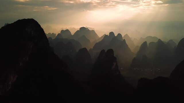 Aerial view of dramatic karst mountains silhouetted against a golden sunset sky with soft mist in Guilin, Guangxi, China.