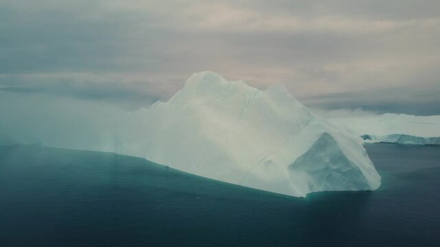 Aerial view of a massive iceberg floating in the dark arctic waters of Greenland.