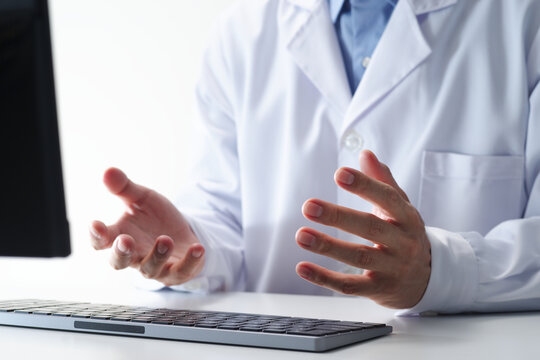 Telemedicine doctor providing remote consultation on computer in medical office. Healthcare professional using telehealth applications for communication, patient monitoring, and virtual healthcare.