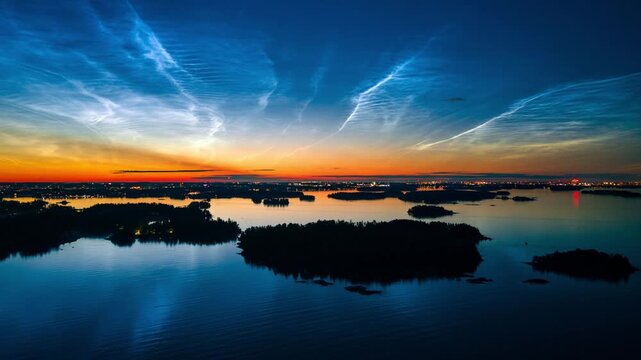 Aerial view of the Espoo archipelago with noctilucent clouds reflecting over calm water and distant city lights on summer night in Espoo, Uusimaa, Finland. Hyperlapse.