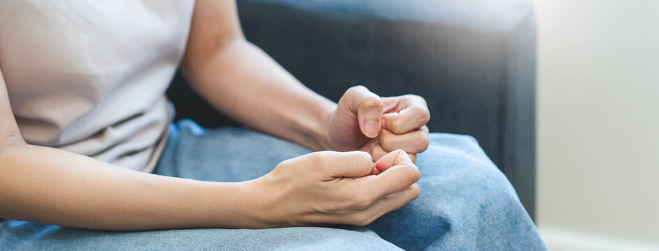 Close up of an anxious woman sitting alone and nervously picking the skin on her fingers, concept of stress, anxiety disorder, dermatillomania, and mental health struggles