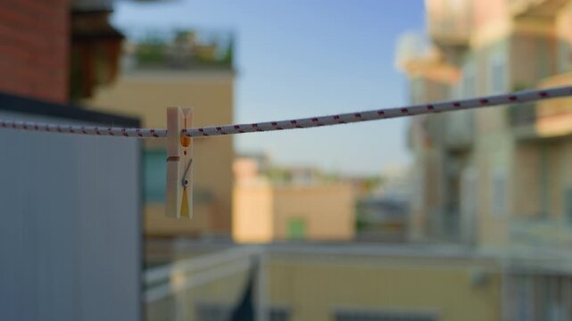 Clothespin laundry line sunset balcony, static handheld close up. Warm evening daylight view of clothes peg on wire with blurred houses background.