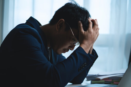 Stressed Businessman Holding His Head While Working at Office Desk, Representing Heavy Workload, Deadline Pressure and Workplace Burnout. Stressed Businessman 