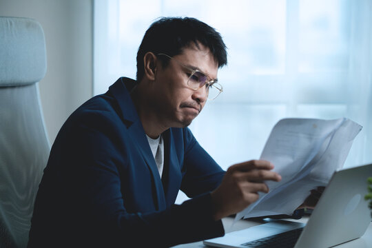 Stressed Businessman Sitting at Office Desk and Holding His Head While Working on Laptop, Showing Workplace Pressure and Frustration