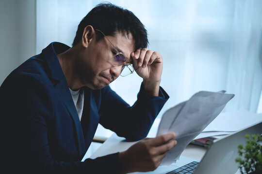 Stressed Businessman Sitting at Office Desk and Holding His Head While Working on Laptop, Showing Workplace Pressure and Frustration