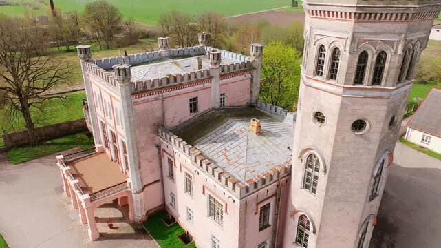 Aerial view historic building with latvian flag waving on sunny day, ancient architecture and lush green landscape.