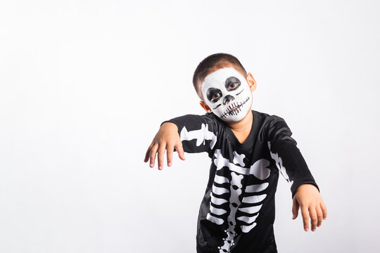 Halloween kid wearing skeleton costume smiling while posing for camera during autumn holiday event inside studio with isolated white background