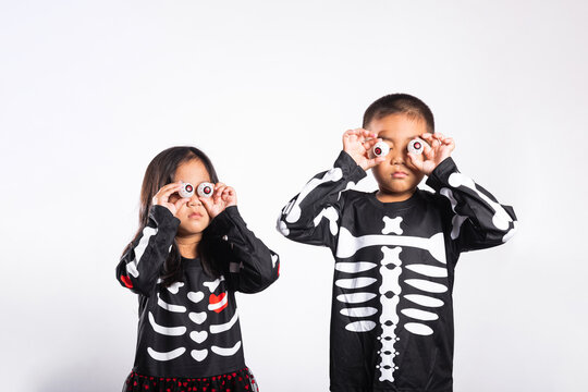 Halloween day, kid holding funny eyes in costume, celebrating holiday party with white background, young boy and girl wearing skeleton outfit, playful autumn festival spirit