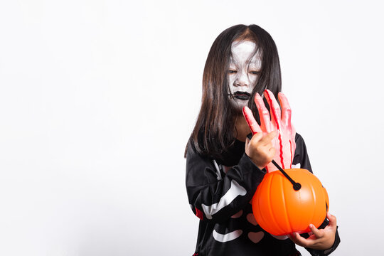 Halloween costume worn by young kid holding spooky fake hand and orange pumpkin bucket against bright white background during autumn holiday celebration for fun seasonal festival imagery