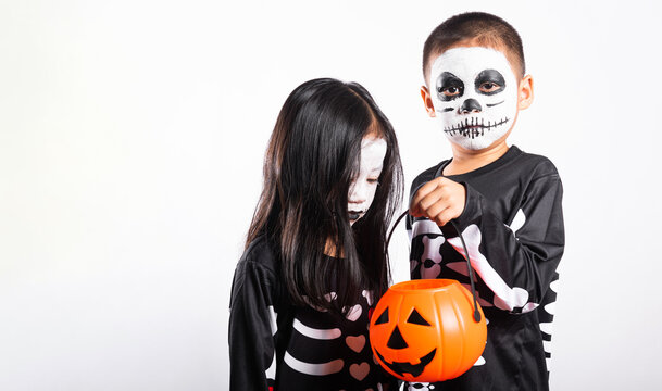 Halloween kids wearing skeleton costumes and face paint holding pumpkin bucket while celebrating holiday event against white isolated background studio setup