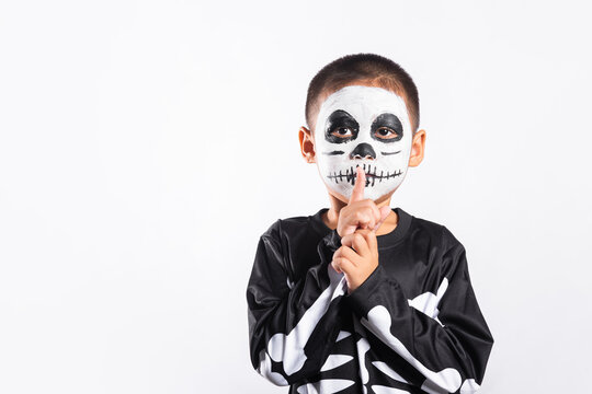 Halloween costume on young kid wearing face paint posing with finger on mouth, standing against white background for autumn holiday celebration event with spooky seasonal spirit